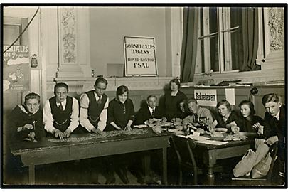 Børnehjælpsdagen 1923. Arbejde med optælling. I baggrunden resultat plakat tegnet af Storm P med angivelse af det indsamlede beløb i 1922. Fotokort u/no.