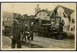 Godstog med mindre damplokomotiv i ukendt skandinavisk by med skilt Frederik Hansen Vine i baggrunden. Fotokort u/no.