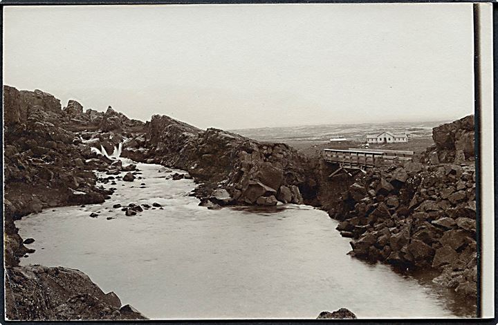Islandsk elv med bro. Hus ses i baggrunden. Fotokort u/no. 