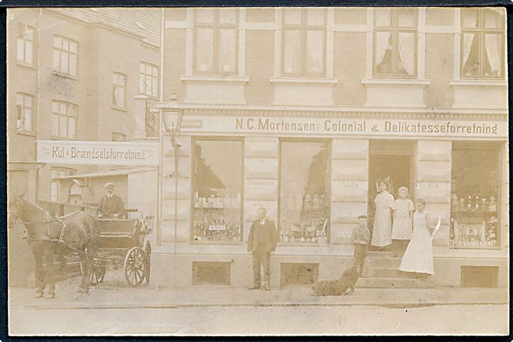 Butiksfacade: Aarhus, Brammersgade 64: N. C. Mortensen - Colonial & Delikatesseforretning samt Kul & Brændselsforretning. Fotokort u/no. 