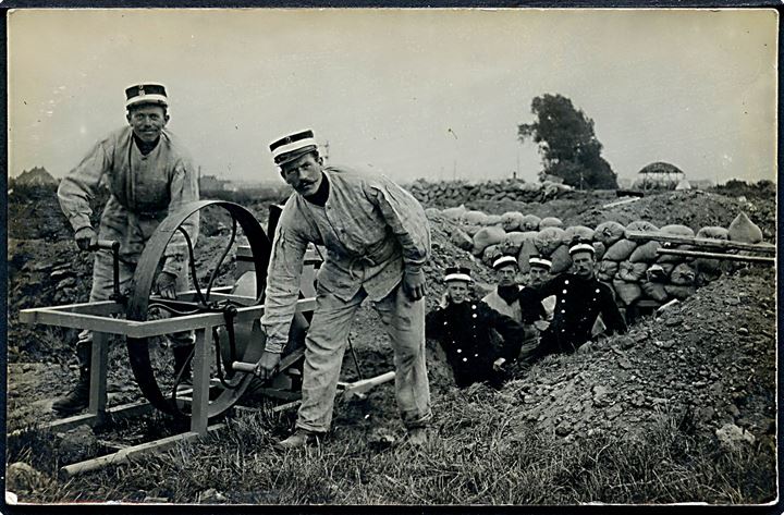 Soldater fra Sikringsstyrken i skyttegrav med slibesten. Fotokort u/no.