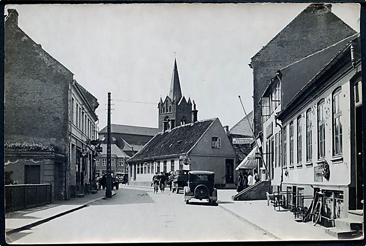 Slagelse, Smedegade med kirke i baggrunden. Fotografi 13x18 cm. Forlæg til fremstilling af postkort fra Robert Olsens Kunstforlag. 