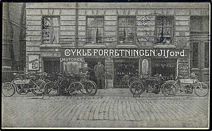 Nørre Allé 9 Cykelforretningen “Ilford” med cykler og motorcykler. Reklamekort sendt som julehilsen 1911. Kvalitet 7