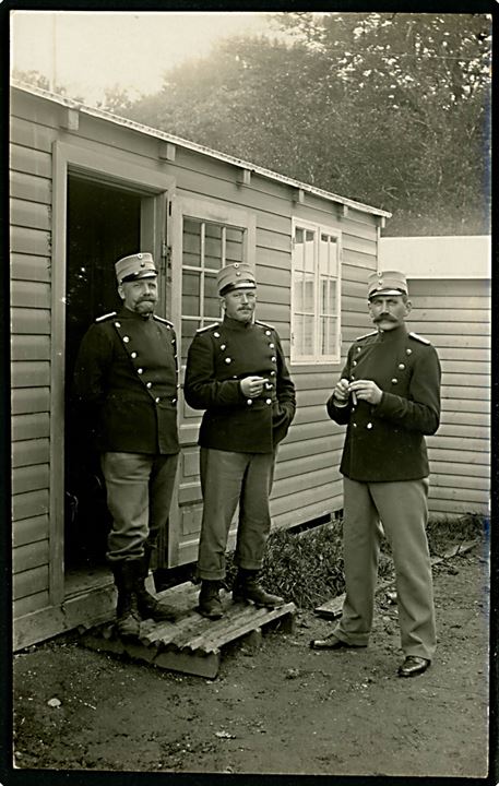 Soldater holder rygepause i baraklejr. Antagelig fra Sikringsstyrken under 1. verdenskrig. Fotokort u/no. Har været opklæbet.