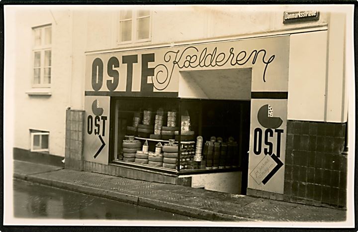 Fredericia. Danmarksstræde med Knud V. Knudsens butik Oste Kælderen. Butikken saboteret i 1944. Ostehandler Knudsen var medlem af DNSAP. Fotokort H. Henriksen, Frederician u/no.