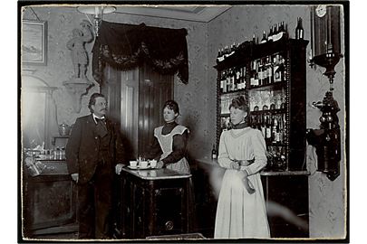 Restauration med tjener, servitricer, spiritus og klassisk telefon. Fotografi (10½x14½ cm) monteret på karton. 