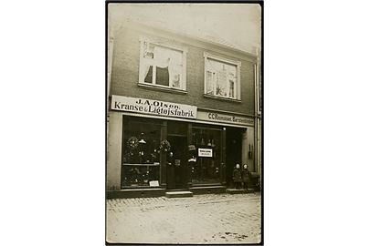 Facade med J. A. Olsen's Kranse & Ligtøjfabrik, samt C. C. Rasmussen's Børstenbinderi. Ukendt by. Fotokort u/no. Har været opklæbet.