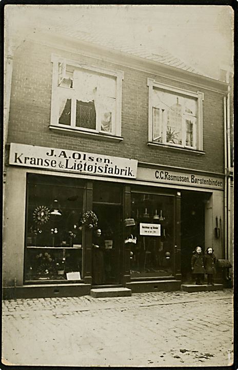 Facade med J. A. Olsen's Kranse & Ligtøjfabrik, samt C. C. Rasmussen's Børstenbinderi. Ukendt by. Fotokort u/no. Har været opklæbet.