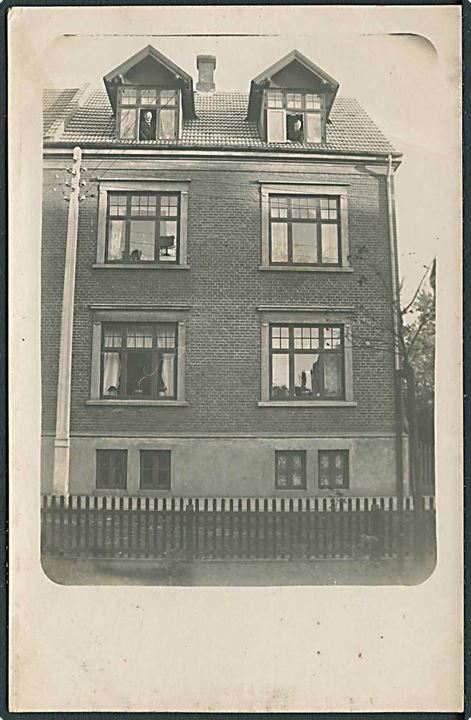 Mand og kvinde i hver deres vindue på øverste etage i stor villa. Anvendt i Vejle. Julen 1914. Foto. 