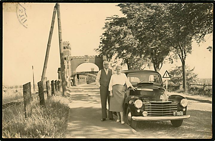 Vauxhall model 1949 med dansk nr.plade R1166 ved jernbanebro over Kieler kanalen. Fotograf Brieschal, Kiel. Sendt fra Stilling 1953 til Aarhus. Kortet viser bagermester Viggo Jensen og hustru Helga under deres udflugt i et nordtyske. 