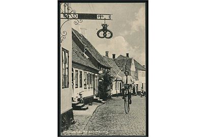 Mand kommer cyklende på en væltepeter ved bageren, Brogade i Ærøskøbing. Hjørneknæk. Stenders no. 94848.