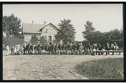 En masse mennesker og heste foran ejendom opført 1898. Fotokort. 