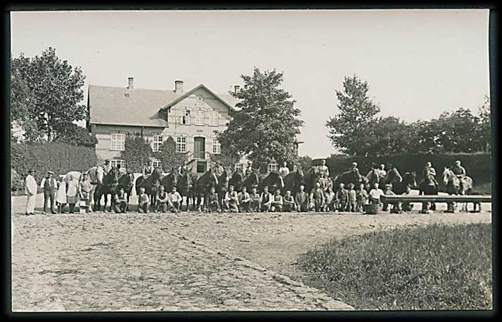 En masse mennesker og heste foran ejendom opført 1898. Fotokort. 