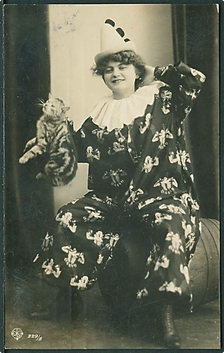 Kvinde iført klovnetøj holder en kat i nakkeskindet. D. L. G. no. 229/8. Fotokort. 