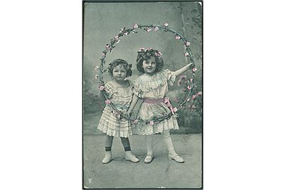 Piger iført hvide kjoler, holder en ring med lyserøde blomster. S. S. B. Serie 2897.