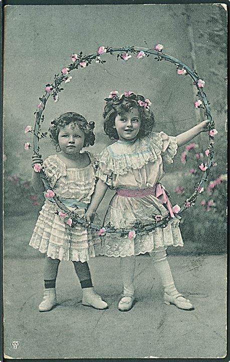 Piger iført hvide kjoler, holder en ring med lyserøde blomster. S. S. B. Serie 2897.