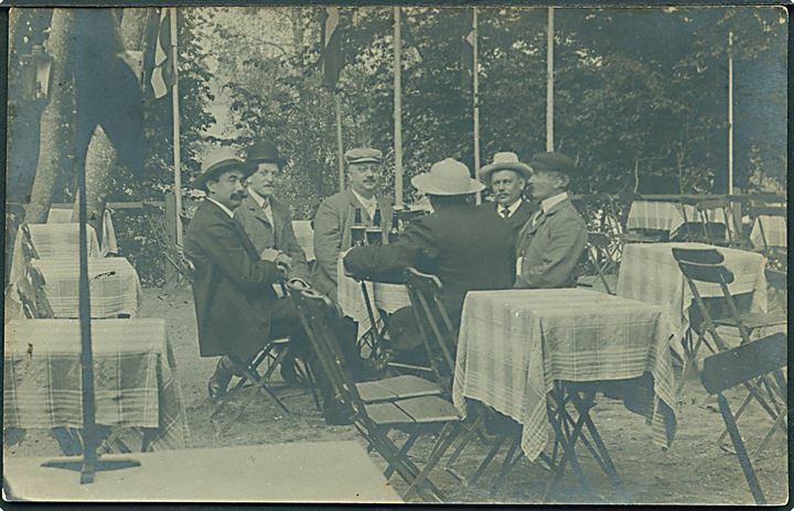 Mænd sidder omkring bord på terrasse. Sted ukendt. Fotokort u/no. 